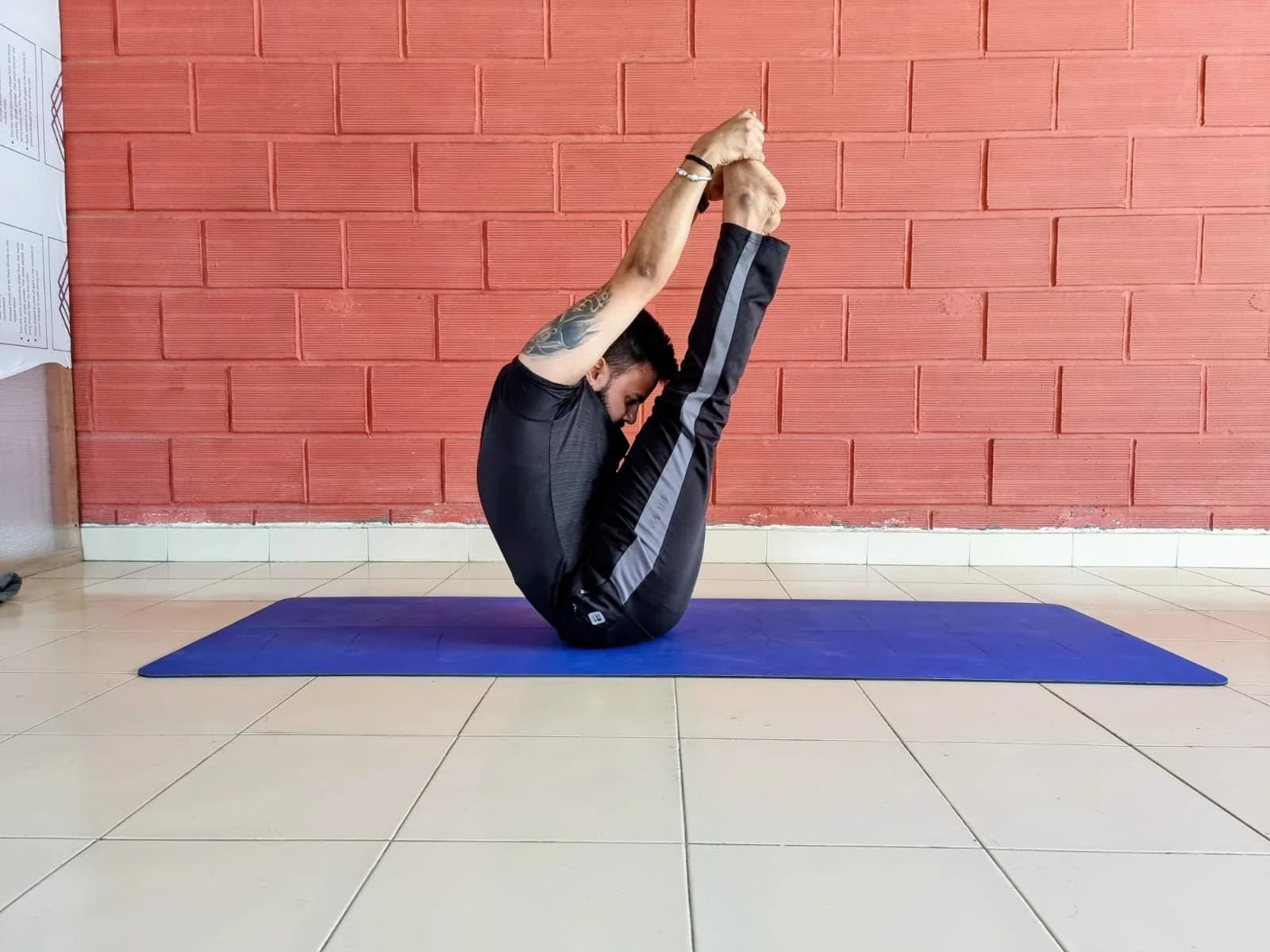Gandharva in a one-legged forward-bend silhouette against a brick wall