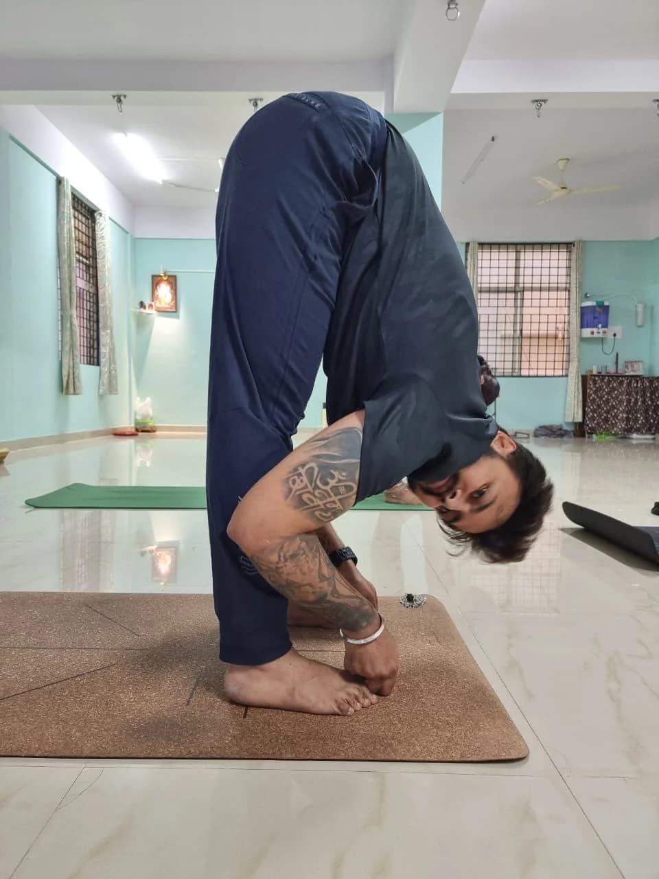 Gandharva in a deep standing forward bend in a home altar room
