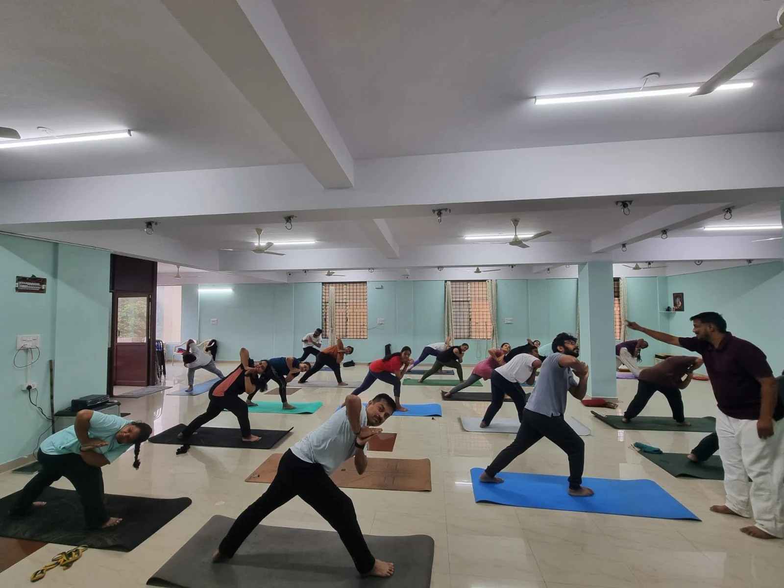 An instructor in a maroon shirt correcting a student's warrior-twist pose