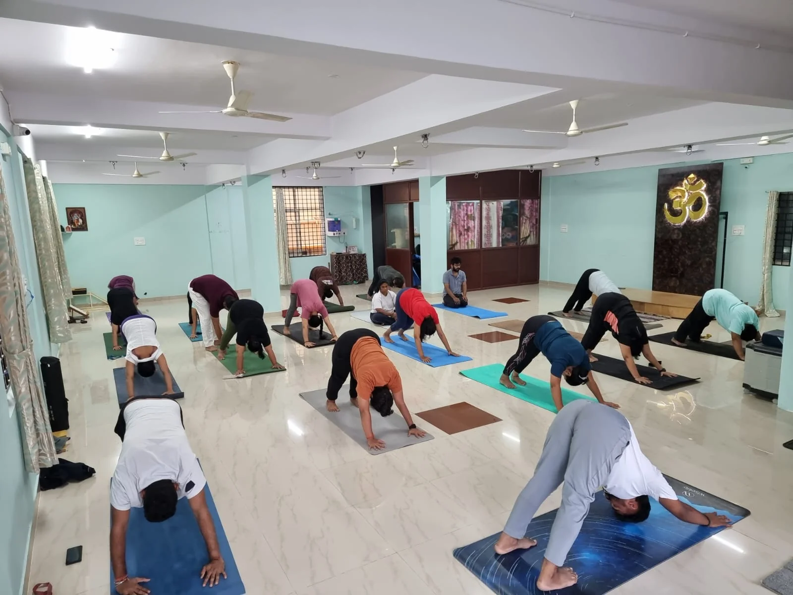 A small casual class in downward-dog beneath a gold Om backdrop
