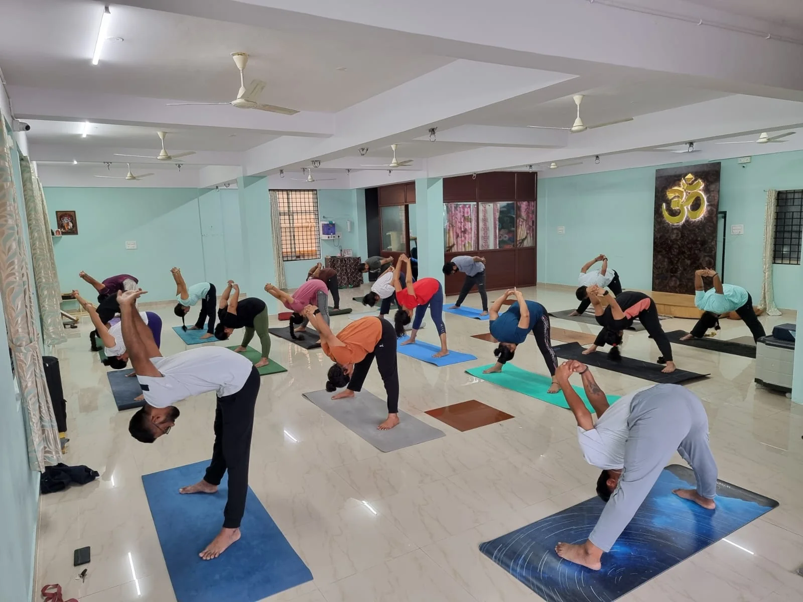A class in a standing forward-fold with hands clasped, gold Om backdrop