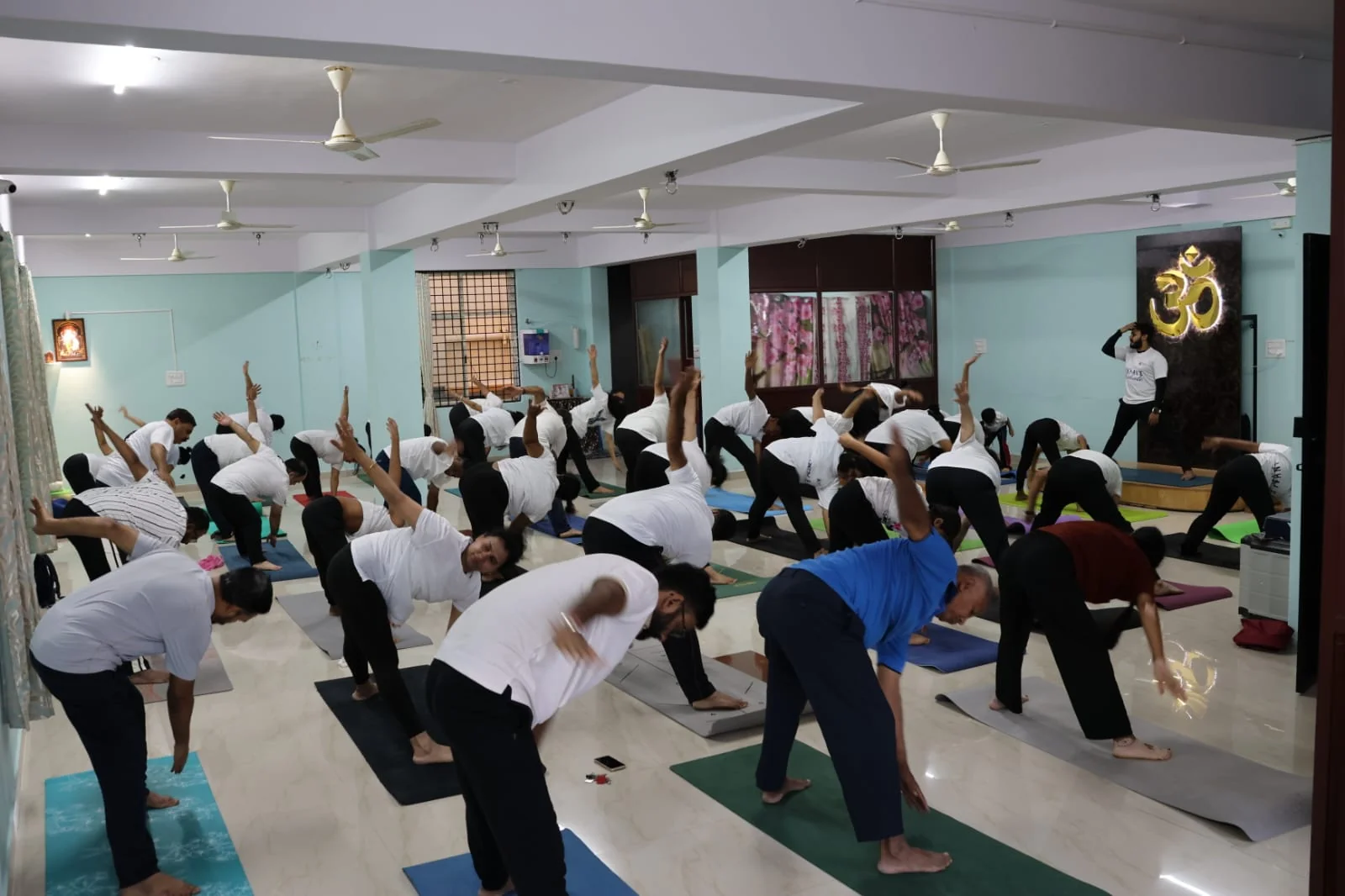 A full class in a side-bend stretch on the studio's wooden platform, gold Om backdrop